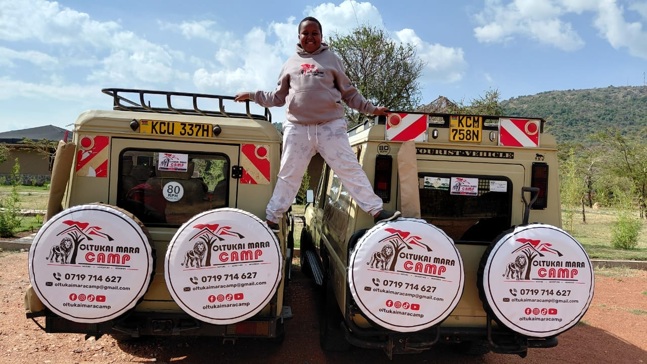 Family safari moment beside branded game-drive vehicles at Oltukai Mara Camp